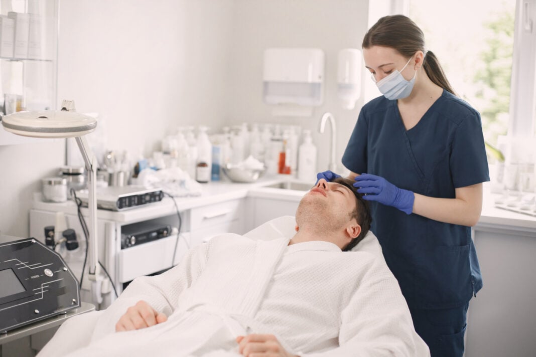 Man lies on a chair and receives a medspa skincare treatment from a young medical professional
